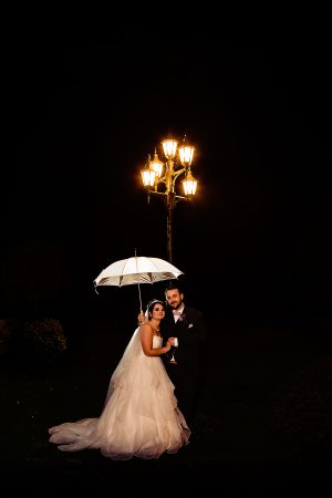 Bride and groom standing under a street light at night holding an umbrella at Rothley Hall Leicestershire